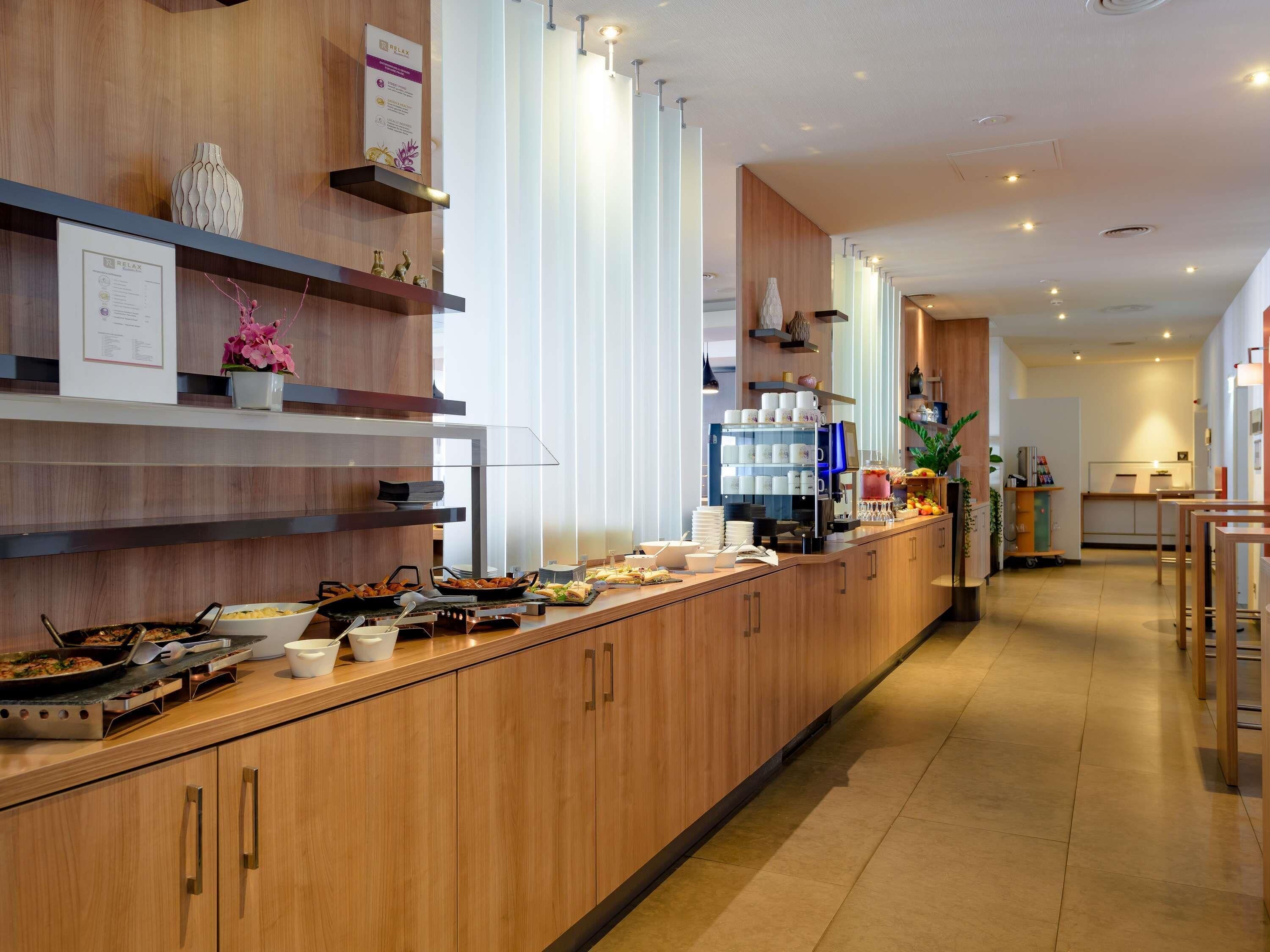 Cocina moderna de hotel con muebles de madera, un mostrador de buffet con diferentes alimentos y una estación de café.