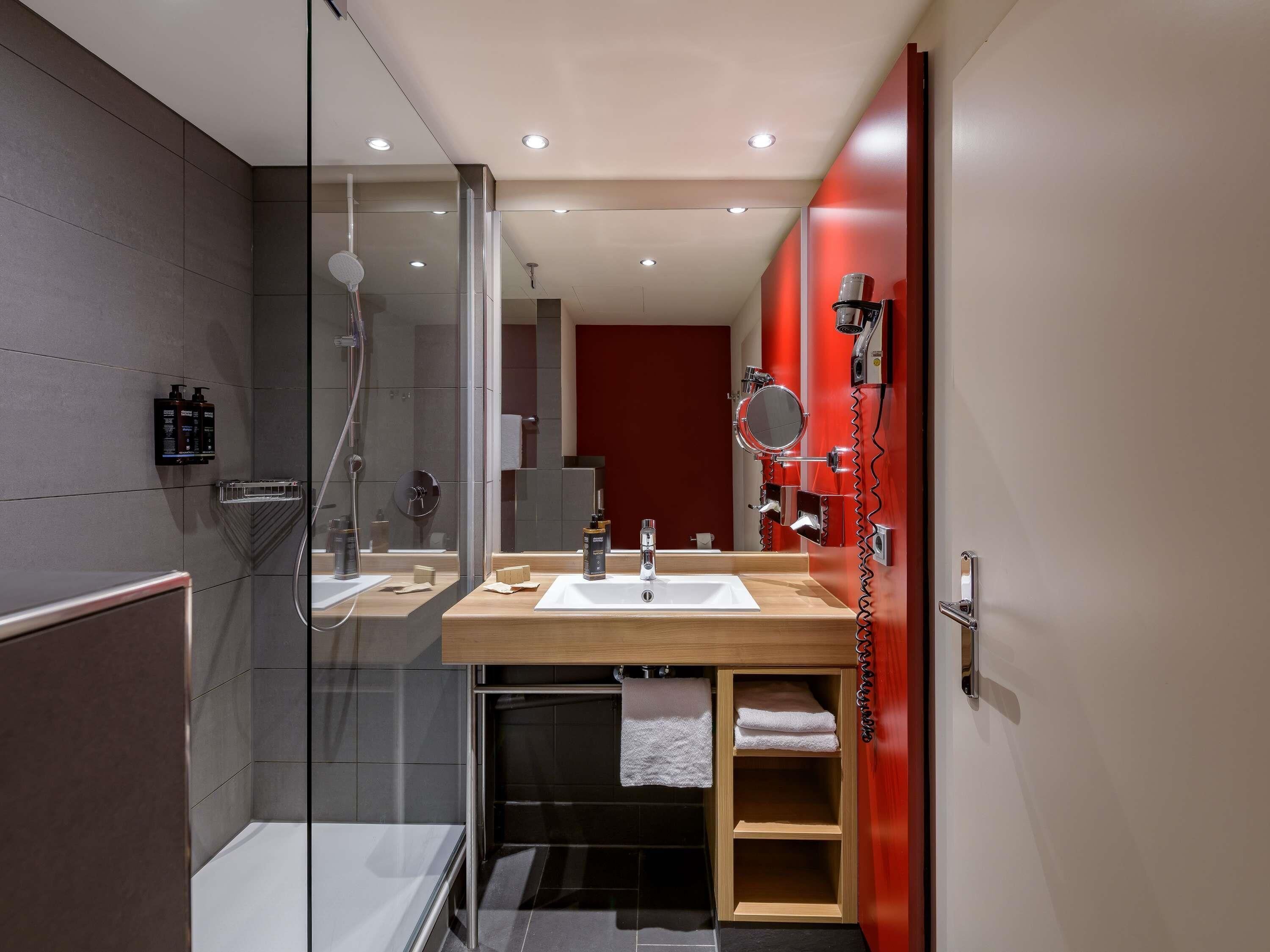 A modern bathroom with a glass shower enclosure, a vanity with a sink, and a red accent wall.