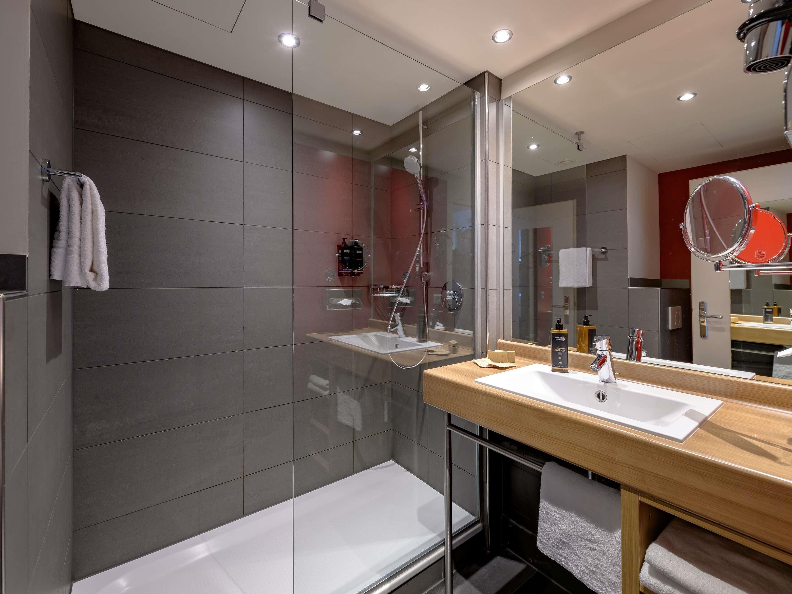 A modern bathroom with a glass shower enclosure, a wooden vanity with a white sink, and a large mirror.