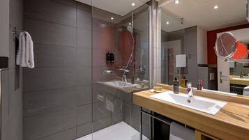 A modern bathroom with a glass shower enclosure, a wooden vanity with a white sink, and a large mirror.