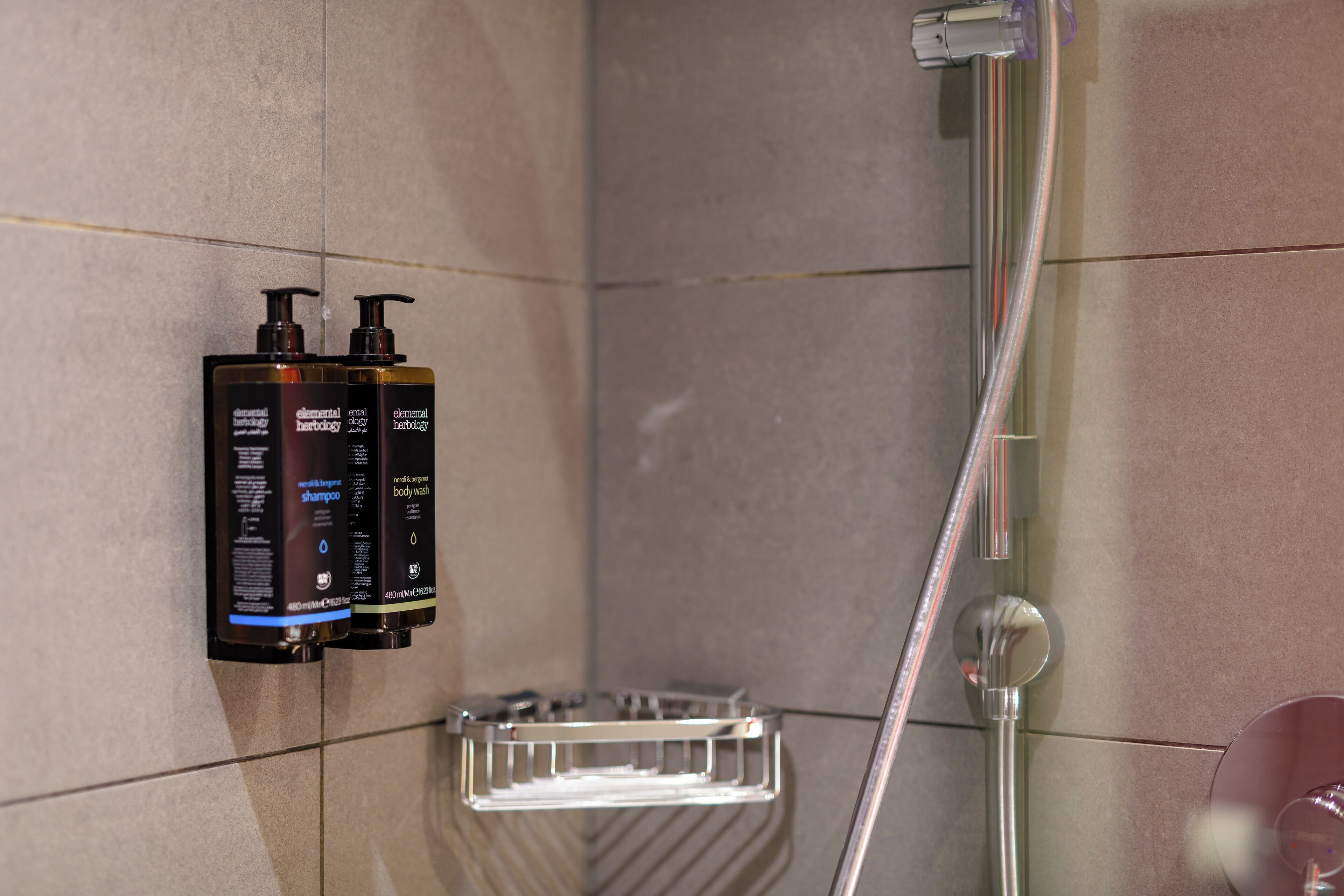 Un baño con ducha, un secador de manos y dos botellas de champú y gel de baño en la pared.