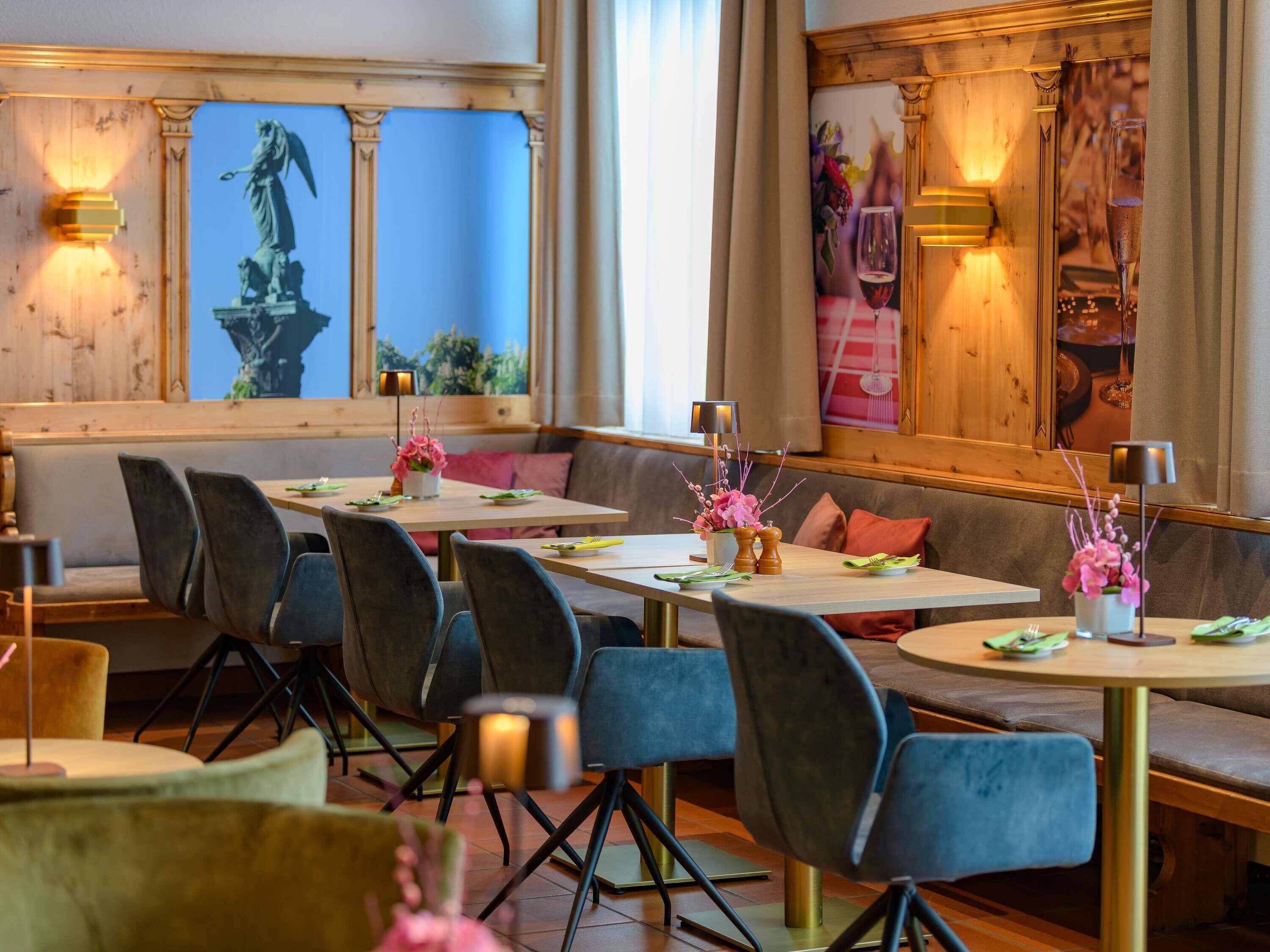 Un restaurante con una larga mesa de comedor, asientos acolchados y flores decorativas.
