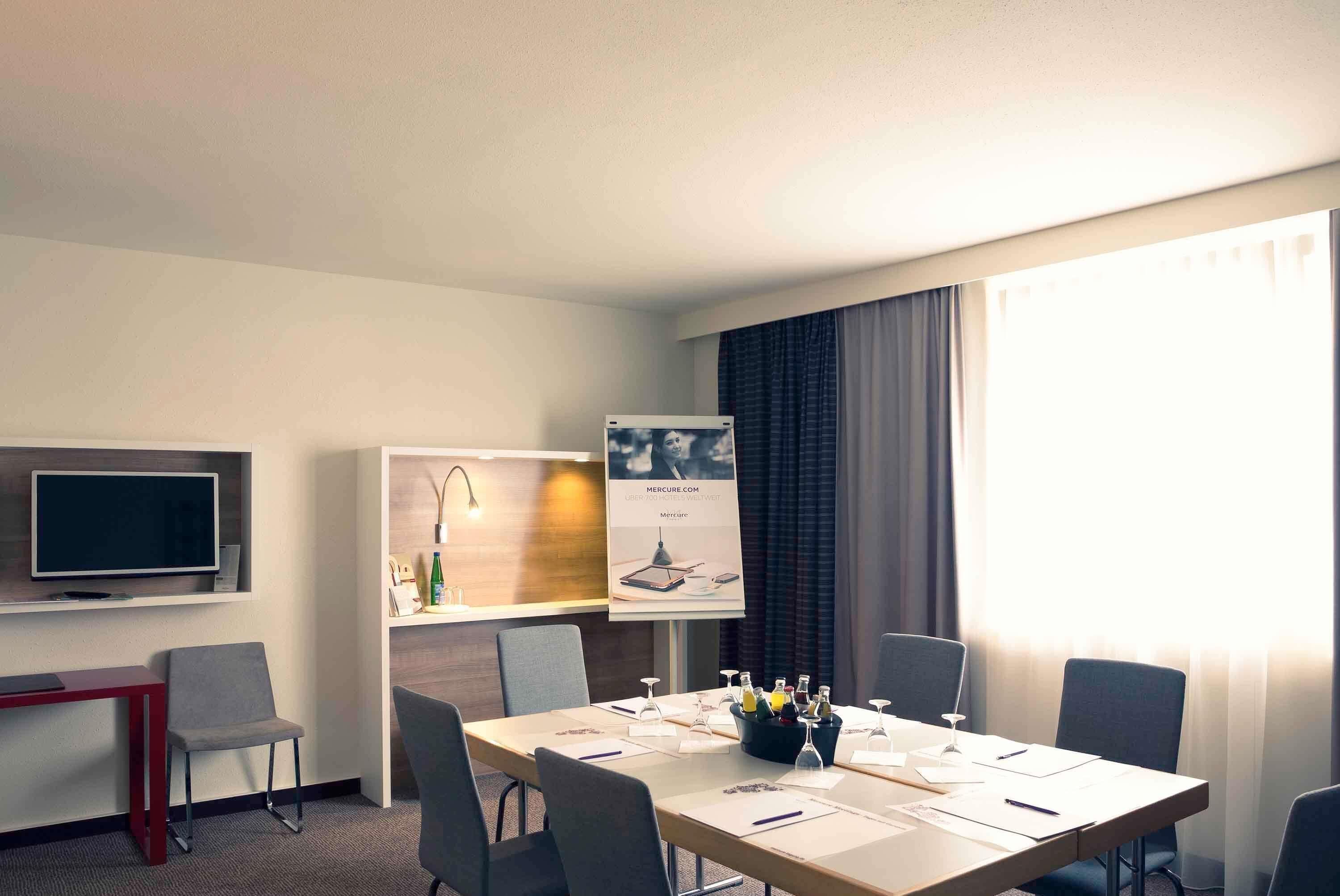 Ein Hotelzimmer mit einem großen Bett, einem Schreibtisch, einem Fernseher, einem Bücherregal und einem Fenster mit Vorhängen.