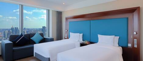 Quarto de hotel com duas camas, um sofá e vista para a cidade.