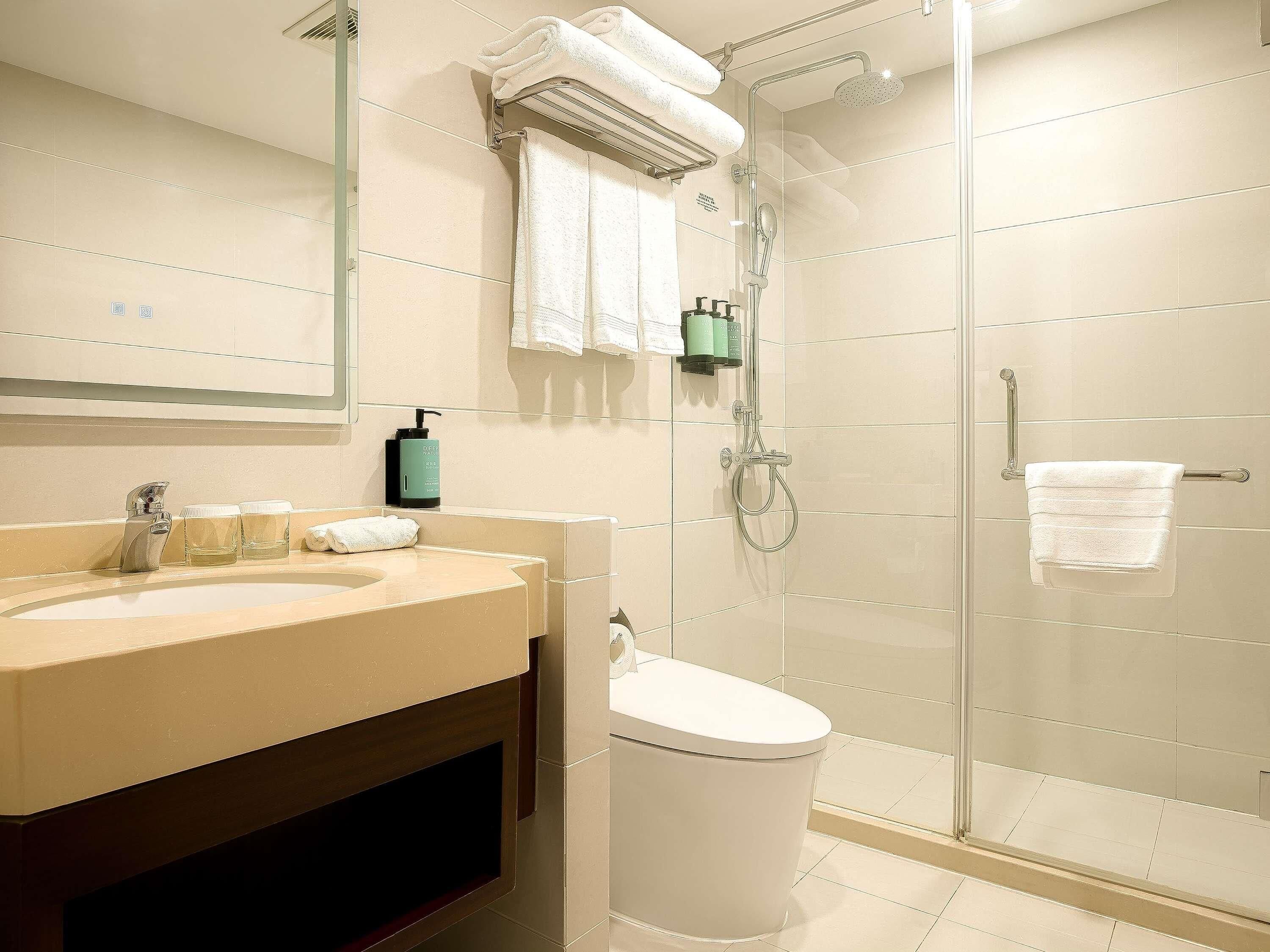 Un baño con lavamanos, espejo, toallero, ducha e inodoro.