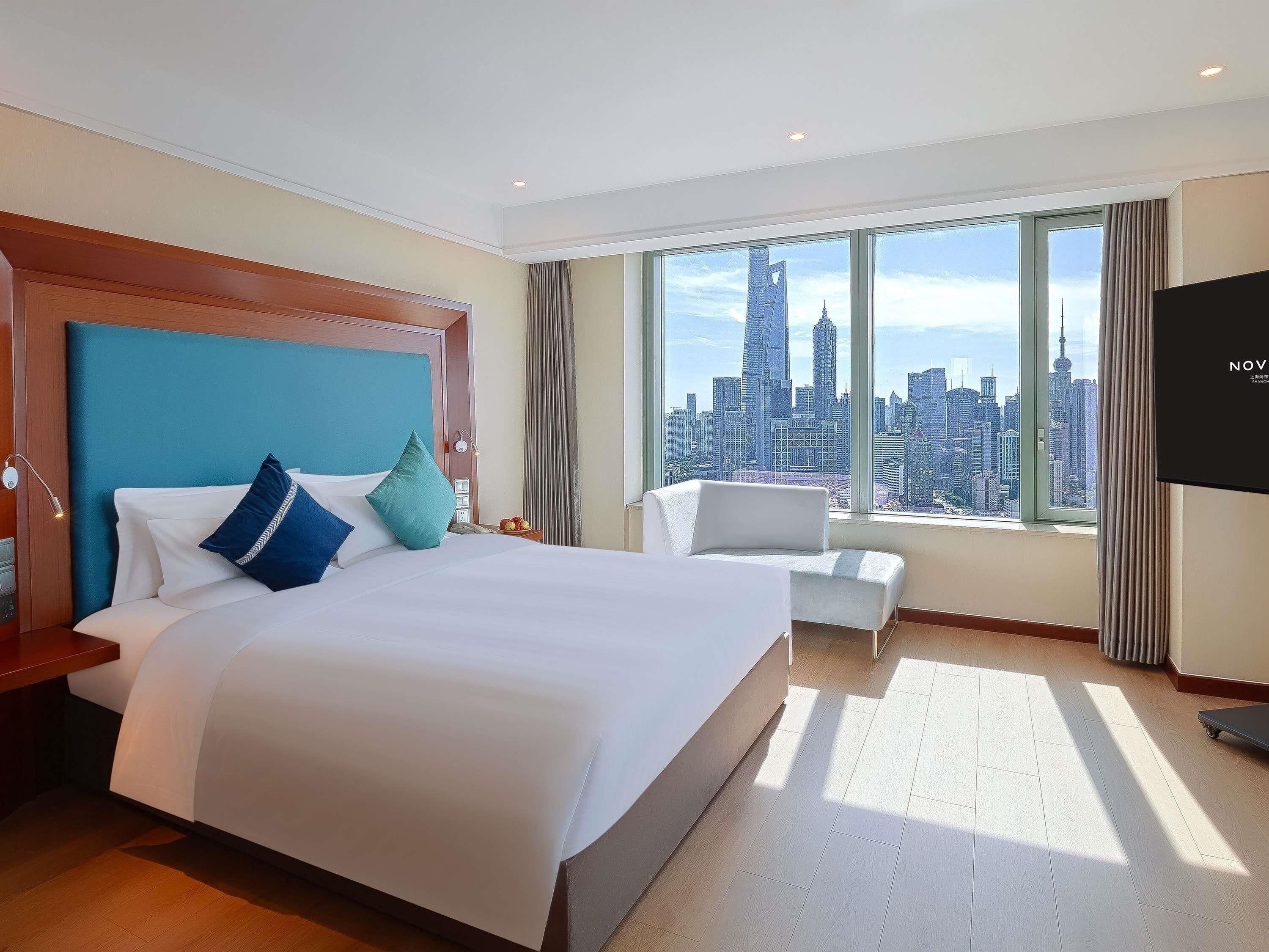 A hotel room with a large bed, a city view, a TV, and a small seating area.