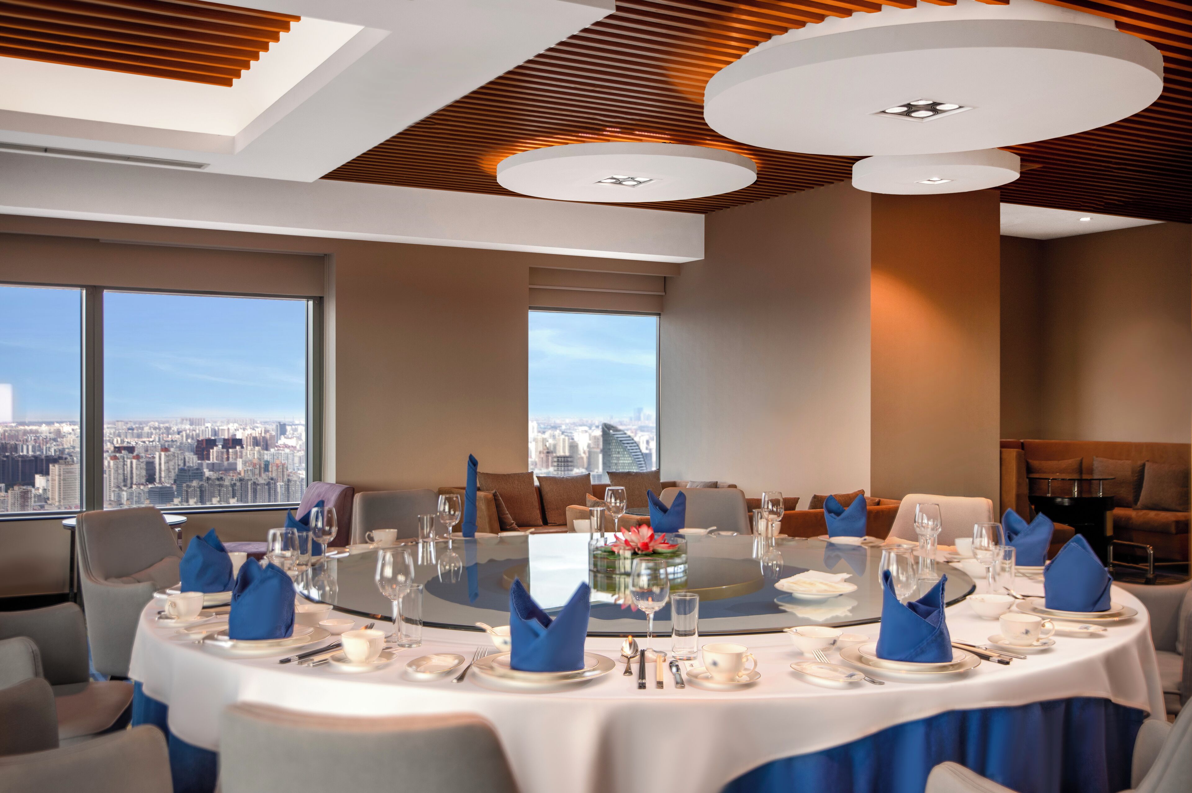 A modern dining room with a panoramic city view, round tables, and blue napkins.