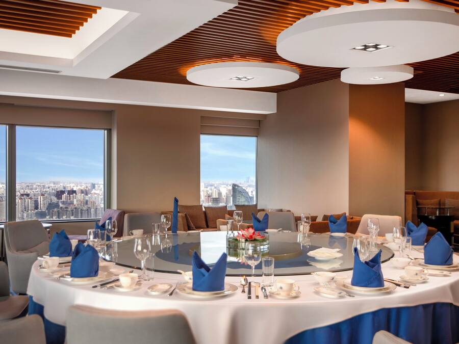 Uma sala de jantar moderna com vista panorâmica da cidade, mesas redondas e guardanapos azuis.