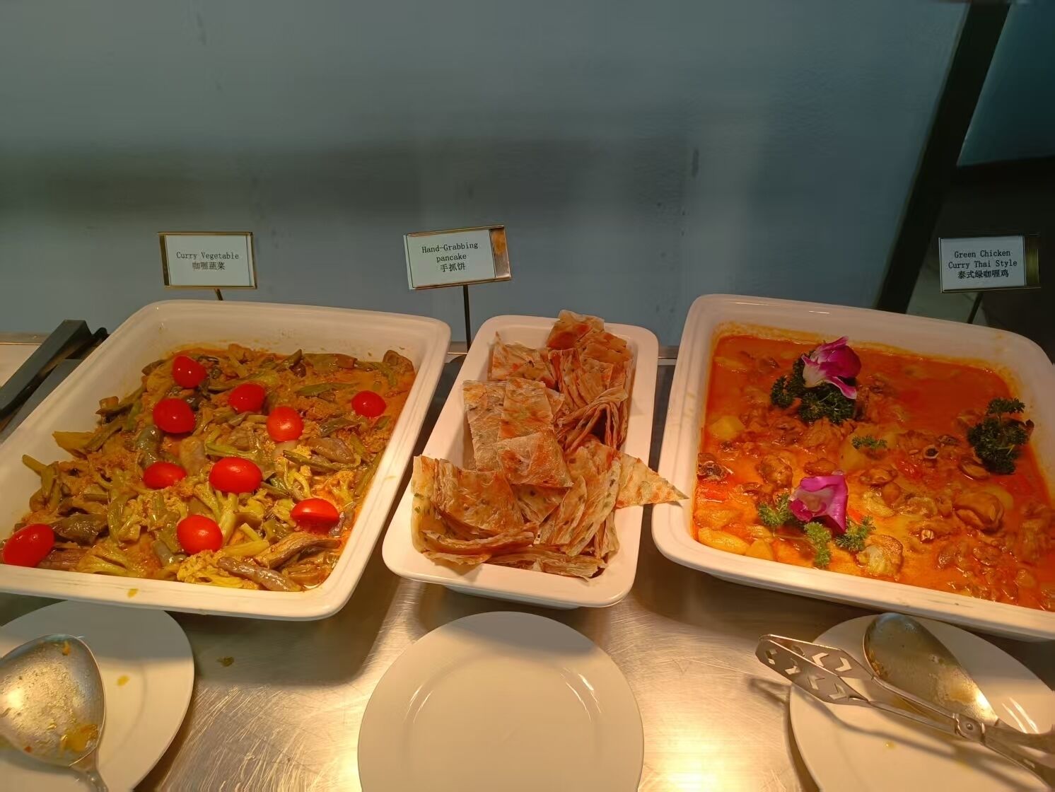 Un bufé con platos etiquetados, incluyendo curry de verduras, panqueque para tomar y curry de pollo verde.