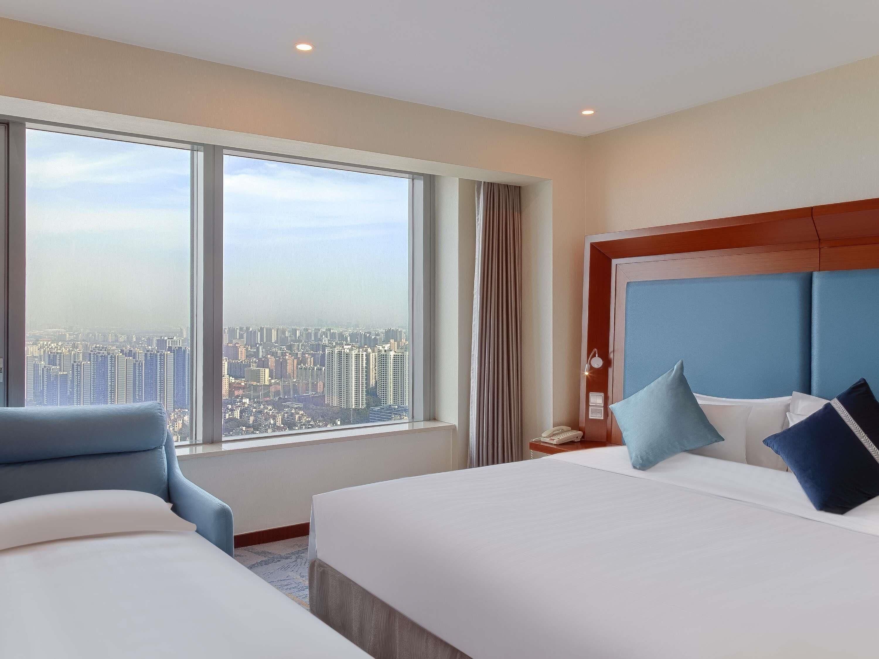 A hotel room with a large window, a bed, a chair, and a nightstand.