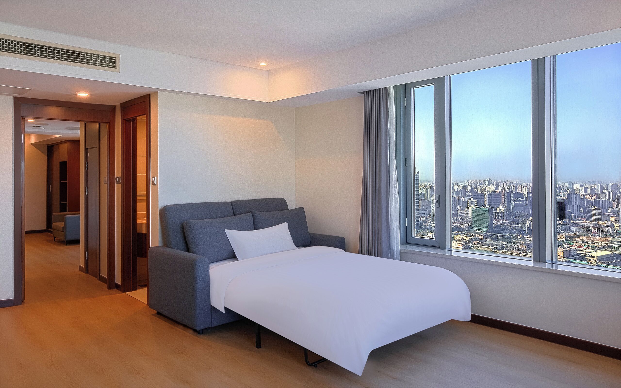 A modern hotel room with a large bed, a view of the city, and a walk-in closet.