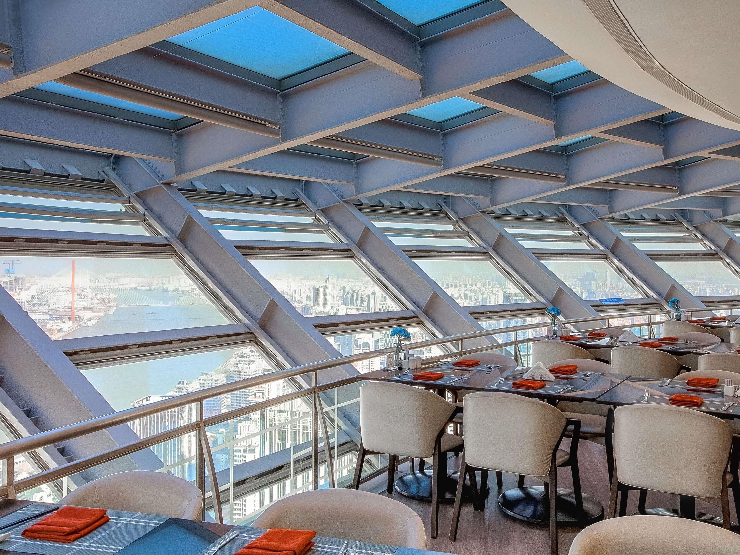 A restaurant with a modern design, featuring a high ceiling with skylights and a view of a cityscape.