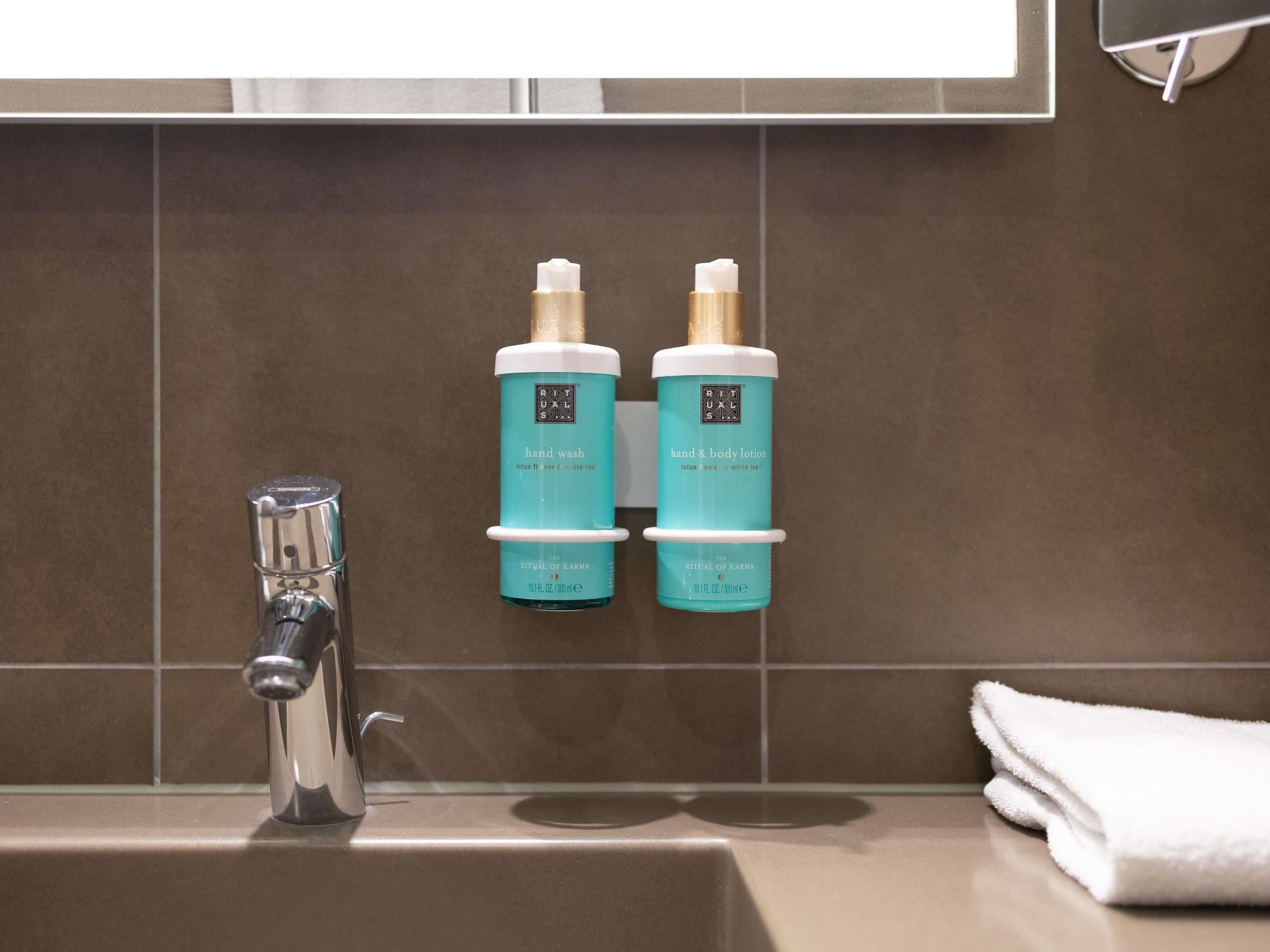 A bathroom with a sink, two bottles of hand wash and body lotion, and a towel.