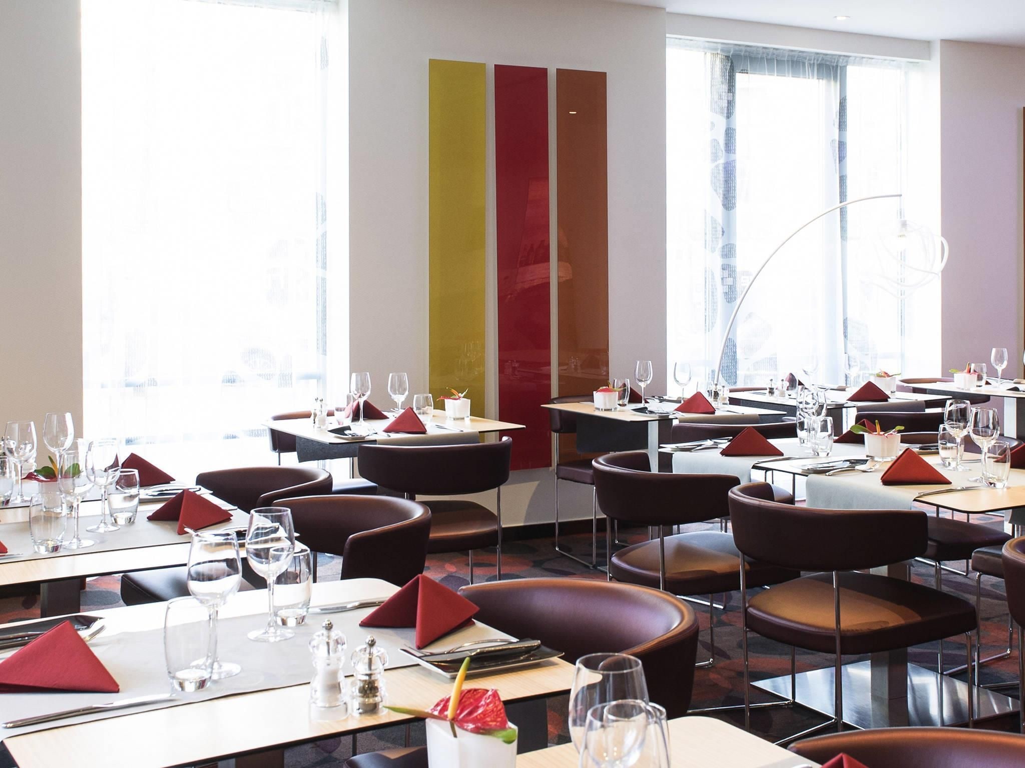 Een modern restaurantinterieur met meerdere eettafels, stoelen en een groot raam dat natuurlijk licht binnenlaat.