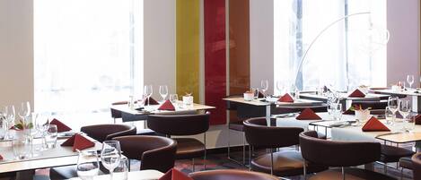 Un interior de restaurante moderno con varias mesas, sillas y un amplio ventanal que proporciona luz natural.