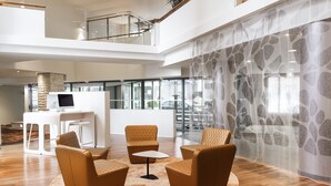 Un'ampia hall con soffitto alto, un'area salotto centrale con divani, un tavolino e una scrivania reception bianca.