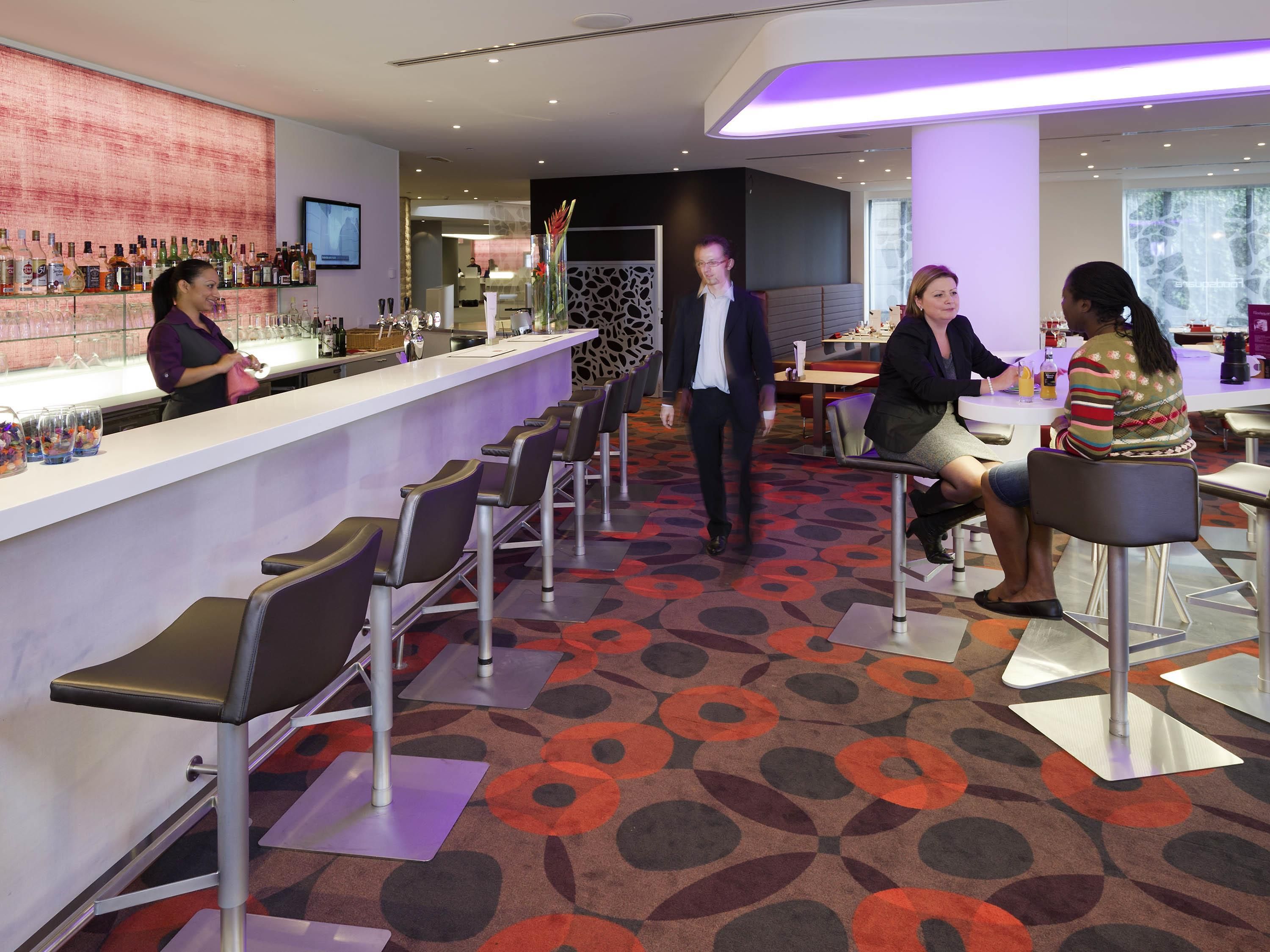 Un espace bar moderne avec un long comptoir, des tabourets de bar et un tapis à motifs.