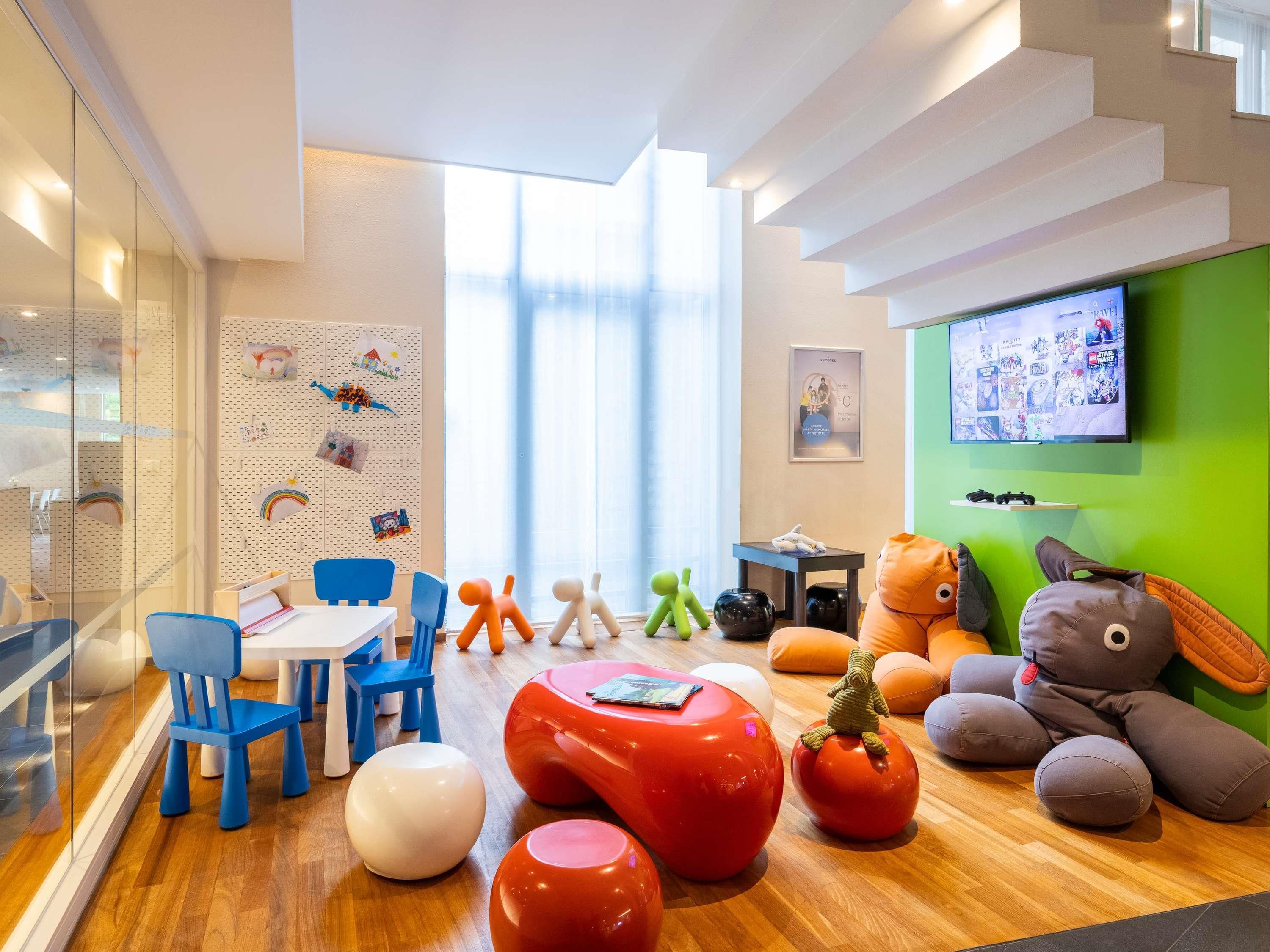 A modern children's play area with colorful furniture, a television, and a wall decorated with children's drawings.