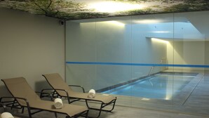 Un'area benessere con piscina vetrata, poltroncine relax e un soffitto decorato con un motivo a tema alberi.