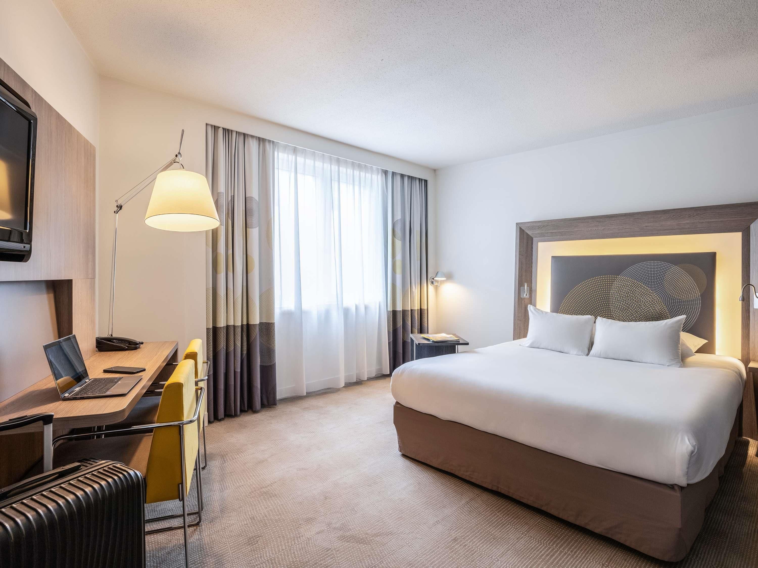 A hotel room with a bed, desk, chair, and a TV.