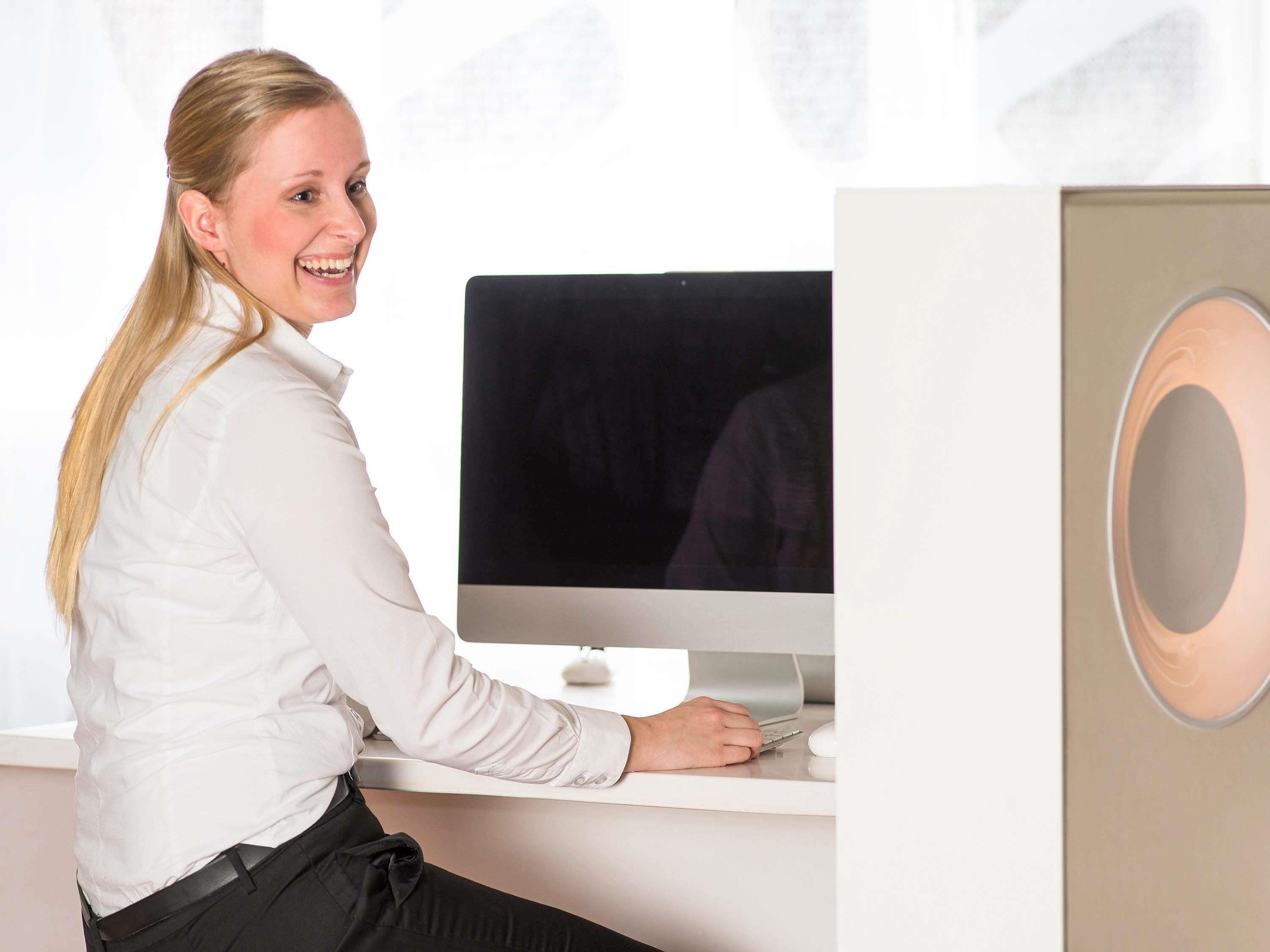 Una persona sentada en un escritorio con una computadora, una silla blanca y un escritorio blanco.
