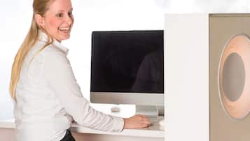 Una persona sentada en un escritorio con una computadora, una silla blanca y un escritorio blanco.