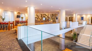 Un hall d’hôtel moderne doté d’une passerelle en verre, d’un espace repas et d’un escalier.