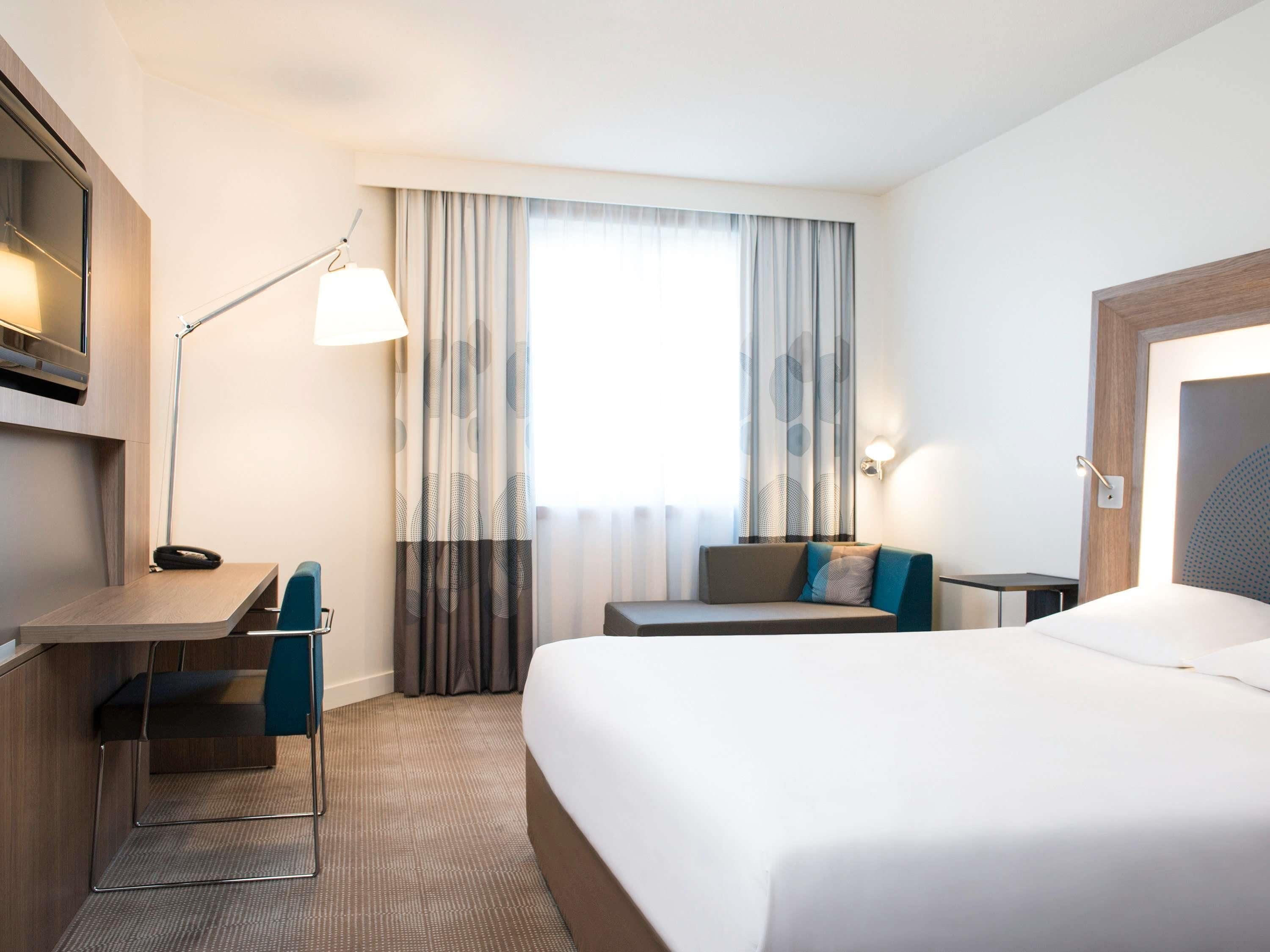 Une chambre d’hôtel équipée d’un lit, d’un bureau, d’une chaise, d’une lampe et de rideaux.