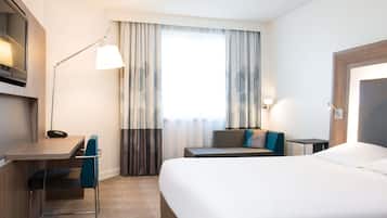 Une chambre d’hôtel équipée d’un lit, d’un bureau, d’une chaise, d’une lampe et de rideaux.