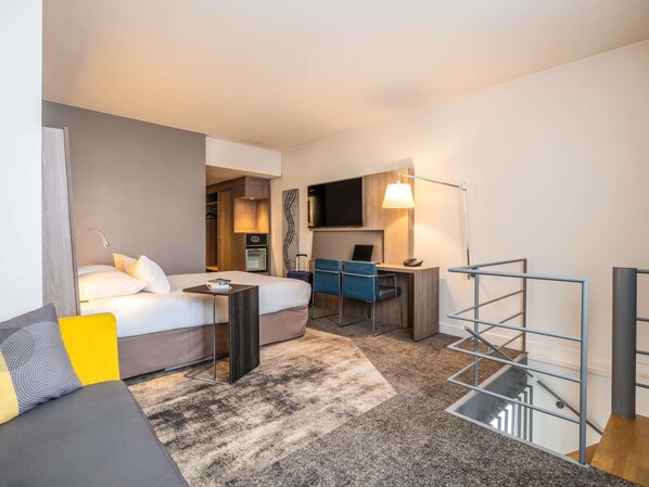 A hotel room with a bed, desk, chair, and a staircase. - Novotel Brussels City Centre (Brussels)