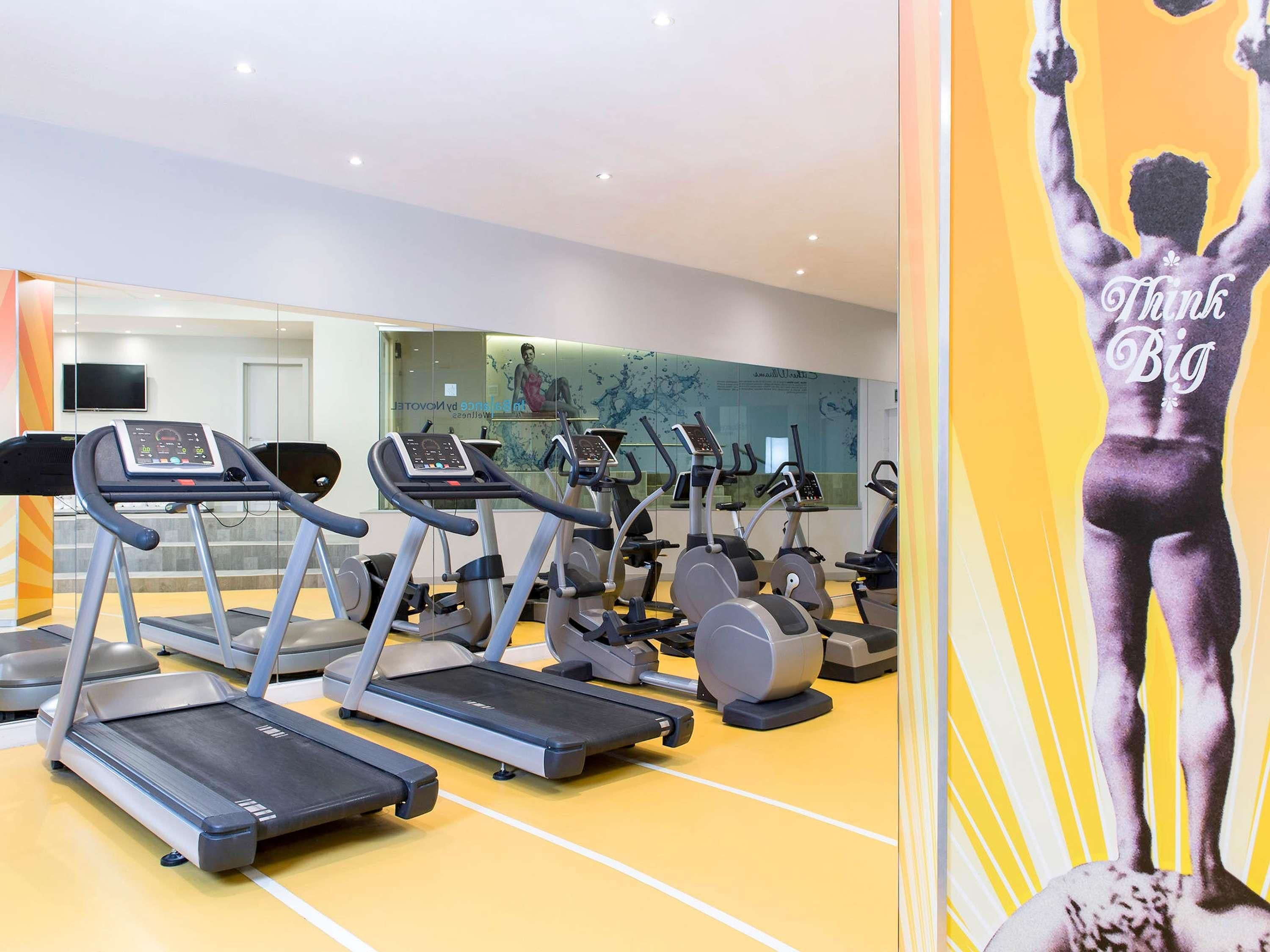A gym with multiple treadmills and elliptical machines, a large mirror, and a motivational poster.