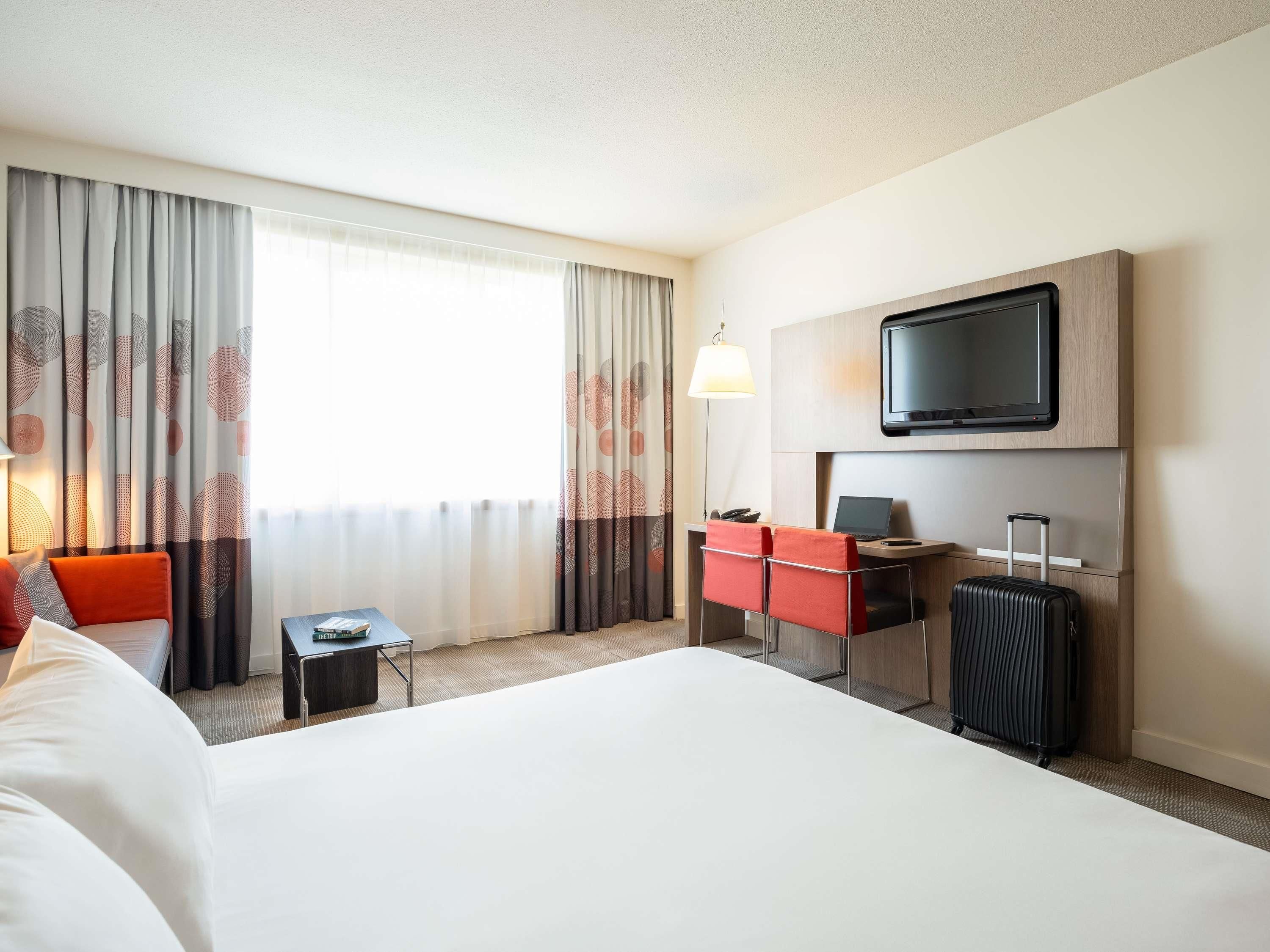 A hotel room with a bed, a desk with a chair, a television, and a suitcase.