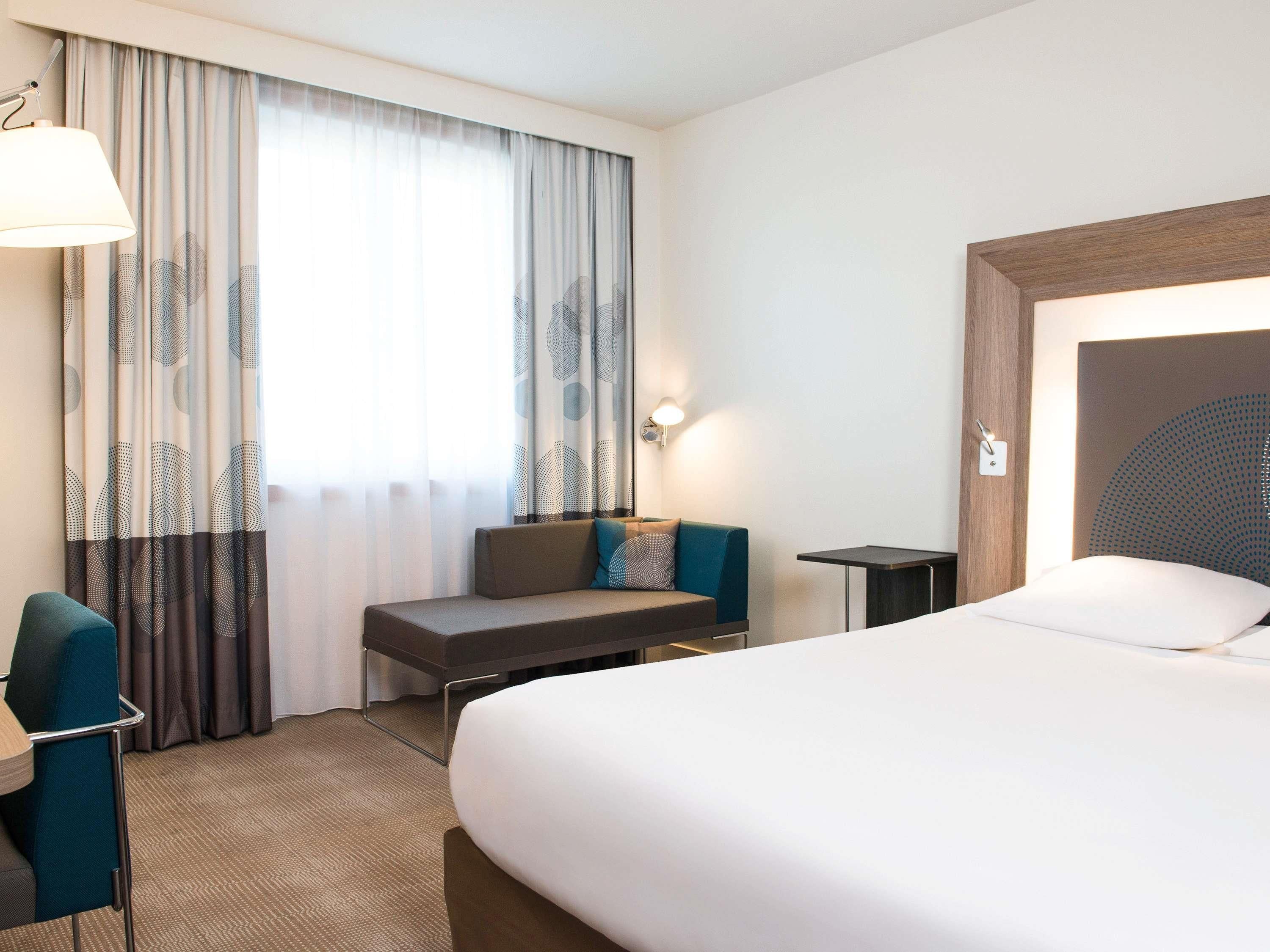 Une chambre d’hôtel avec un lit, un bureau, une chaise, un canapé et une fenêtre avec des rideaux.