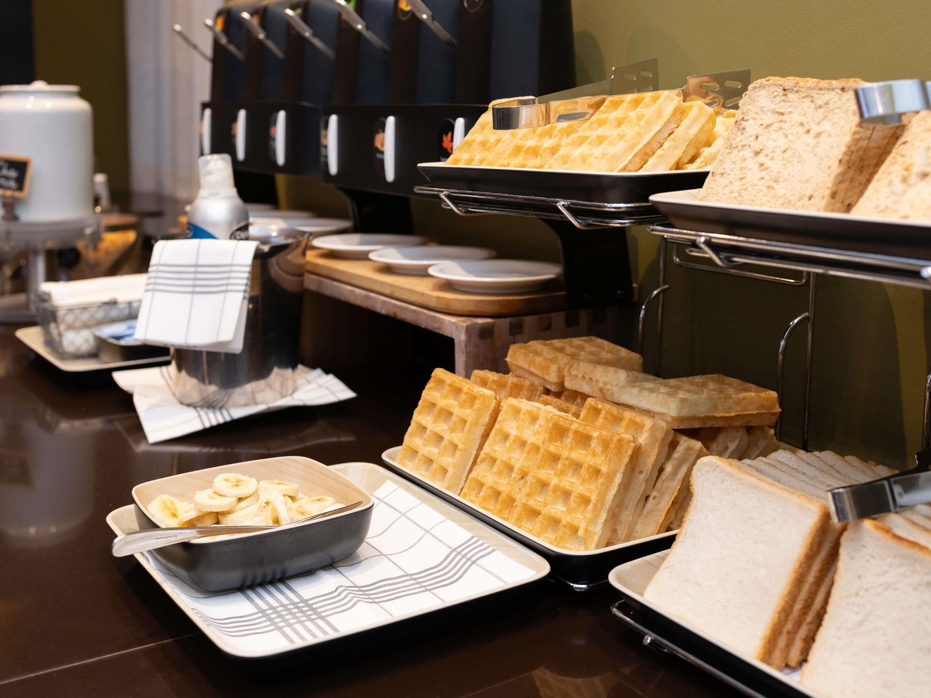 A buffet with waffles, sandwiches, and a bowl of sliced bananas.