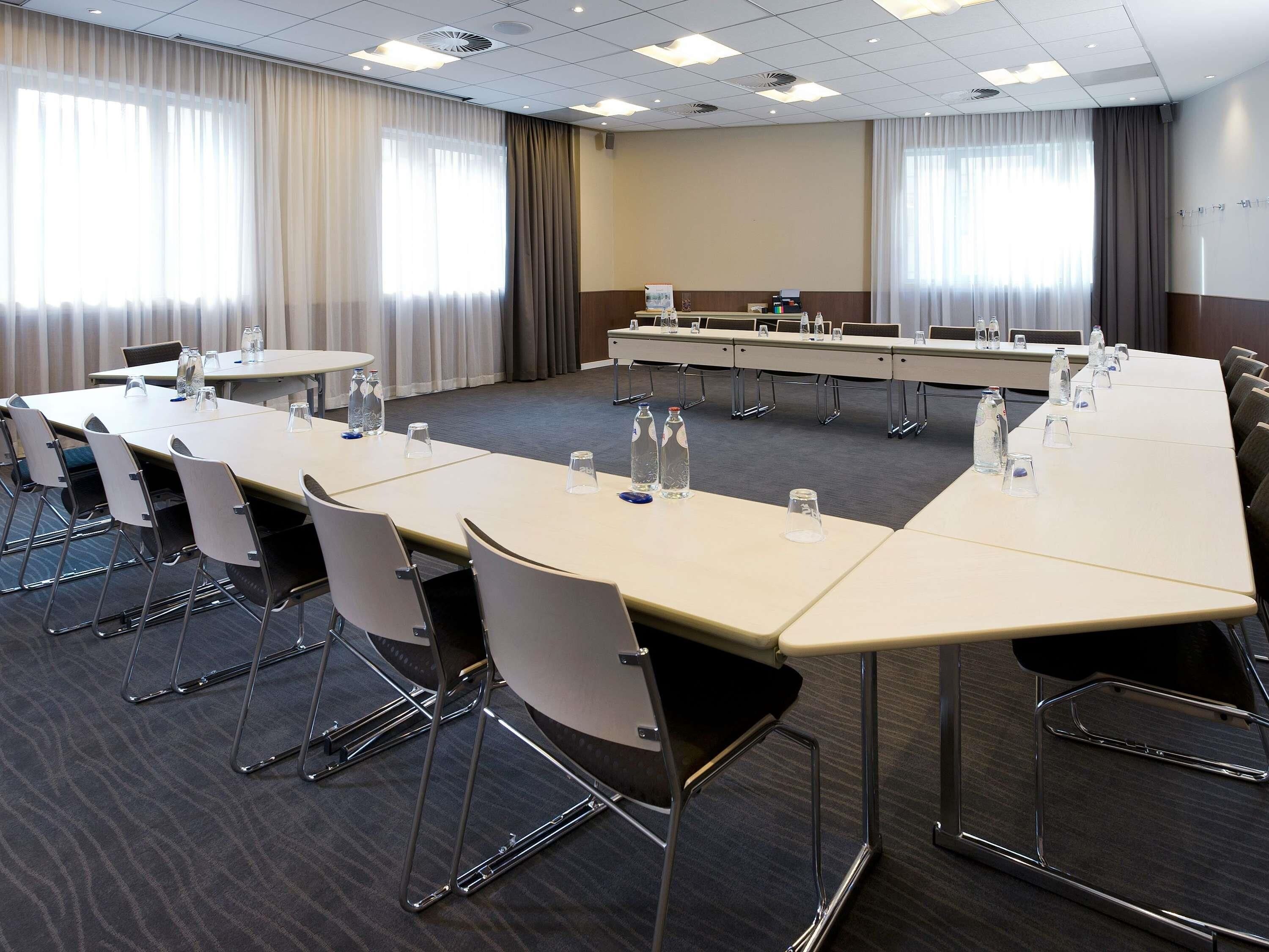 Une salle de conférence avec une longue table, des chaises et des bouteilles d’eau.