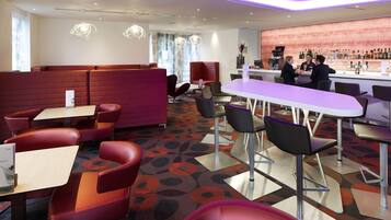 A modern bar area with seating, a bar counter, and a variety of bottles.