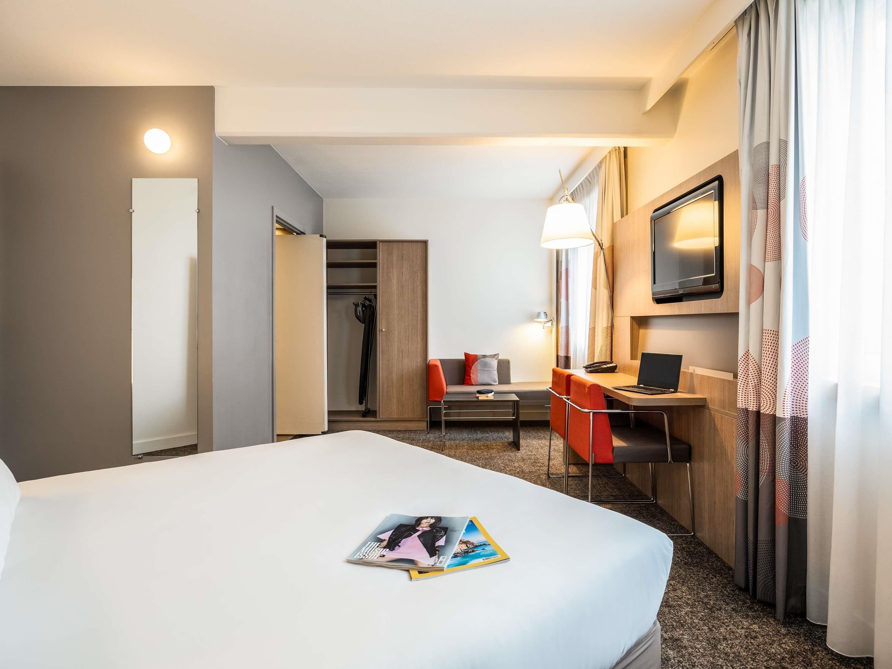 A hotel room with a bed, a desk, a chair, a TV, and a wardrobe.