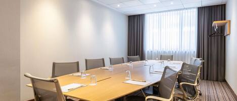 A conference room with a long table, chairs, a projector, and a large window with curtains.