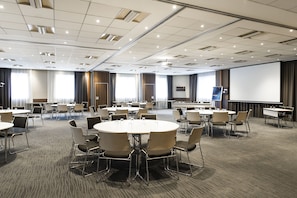 A conference room with round tables and chairs, a large screen, and a projector.