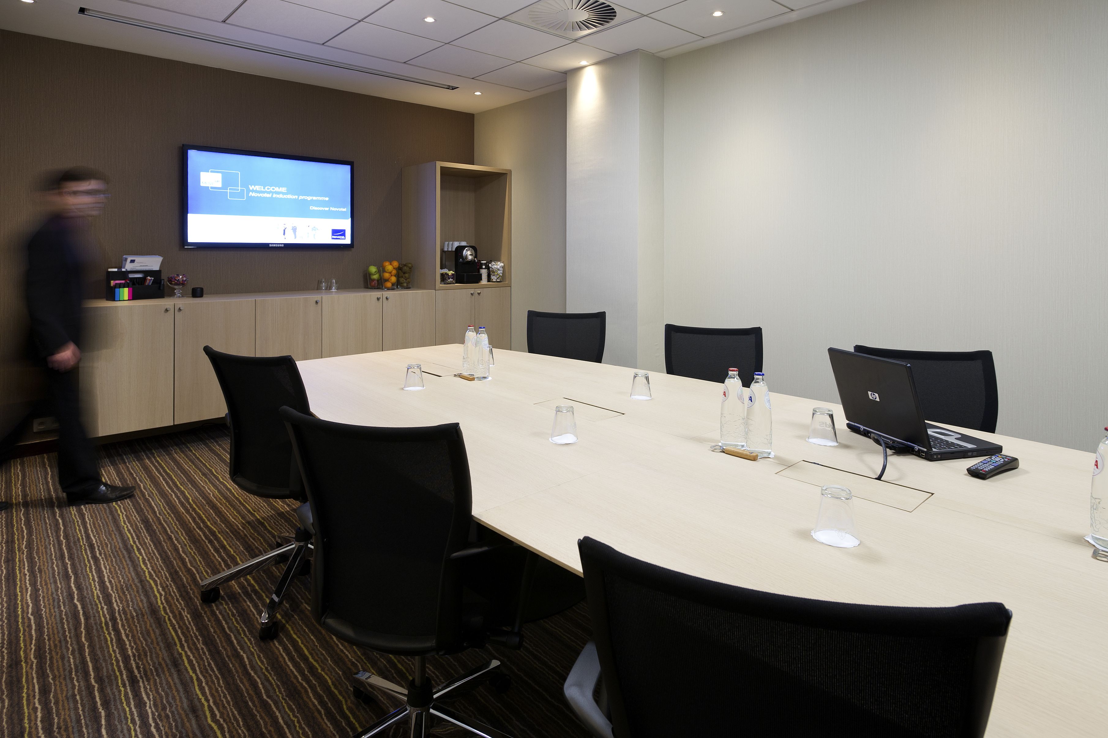 A conference room with a long table, chairs, a projector screen, and a coffee machine.