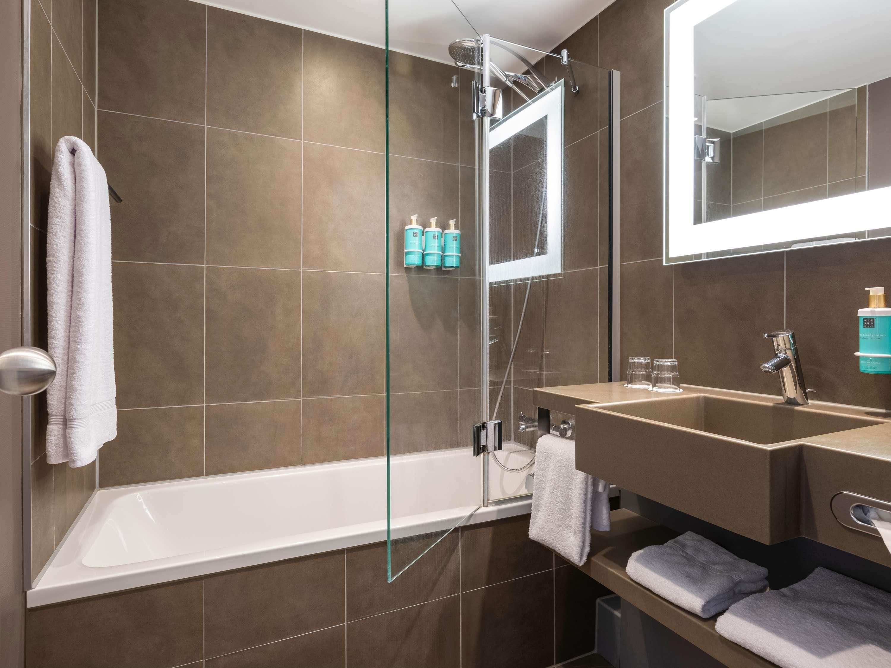 Un baño moderno con ducha envuelta en vidrio, un espejo grande y un mueble de tocador con lavabo y toallero.