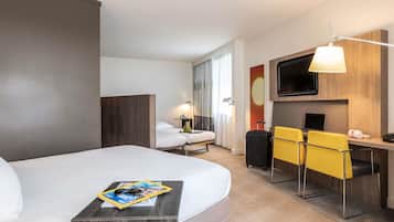 Ett hotellrum med en stor säng, ett skrivbord med en stol, en TV och ett fönster med gardiner.