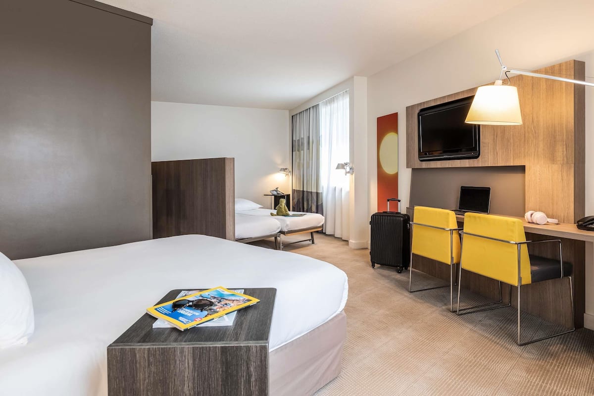 Une chambre d’hôtel avec un grand lit, un bureau avec une chaise, une télévision et une fenêtre avec des rideaux.