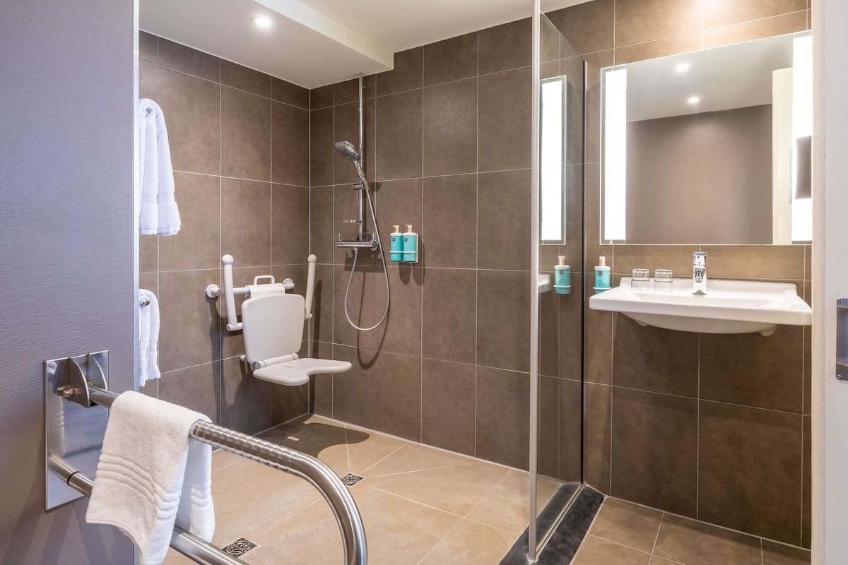 Une salle de bain moderne avec une douche à parois de verre, des toilettes blanches, un lavabo avec un miroir et un porte-serviettes.