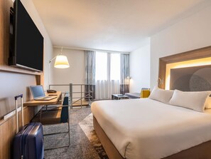 Et hotelværelse med seng, skrivebord, stol, computer, kuffert og et fjernsyn.