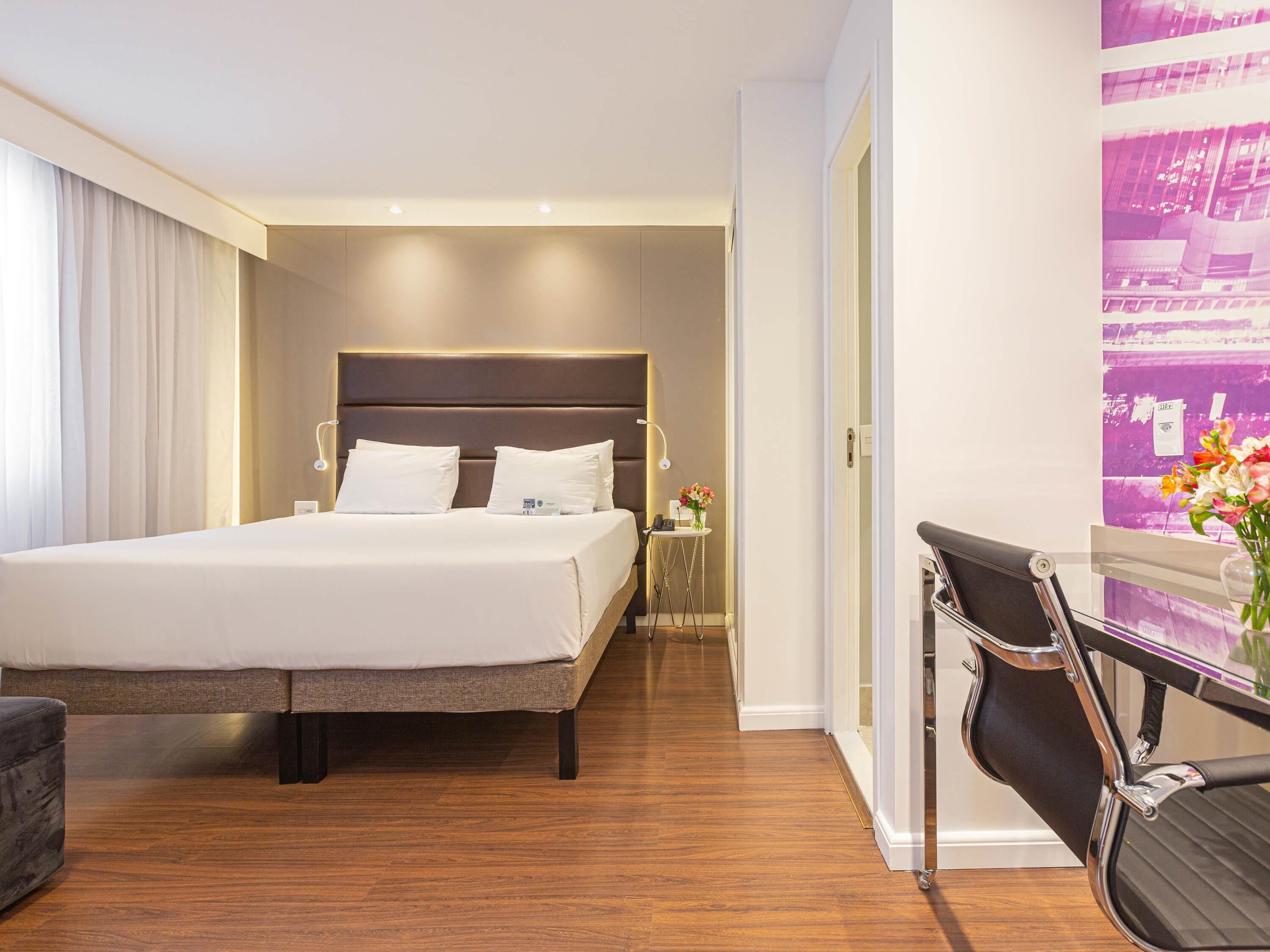 Ein Hotelzimmer mit einem großen Bett, einem Nachttisch, einem Stuhl und einem Schreibtisch mit Sitzgelegenheit.