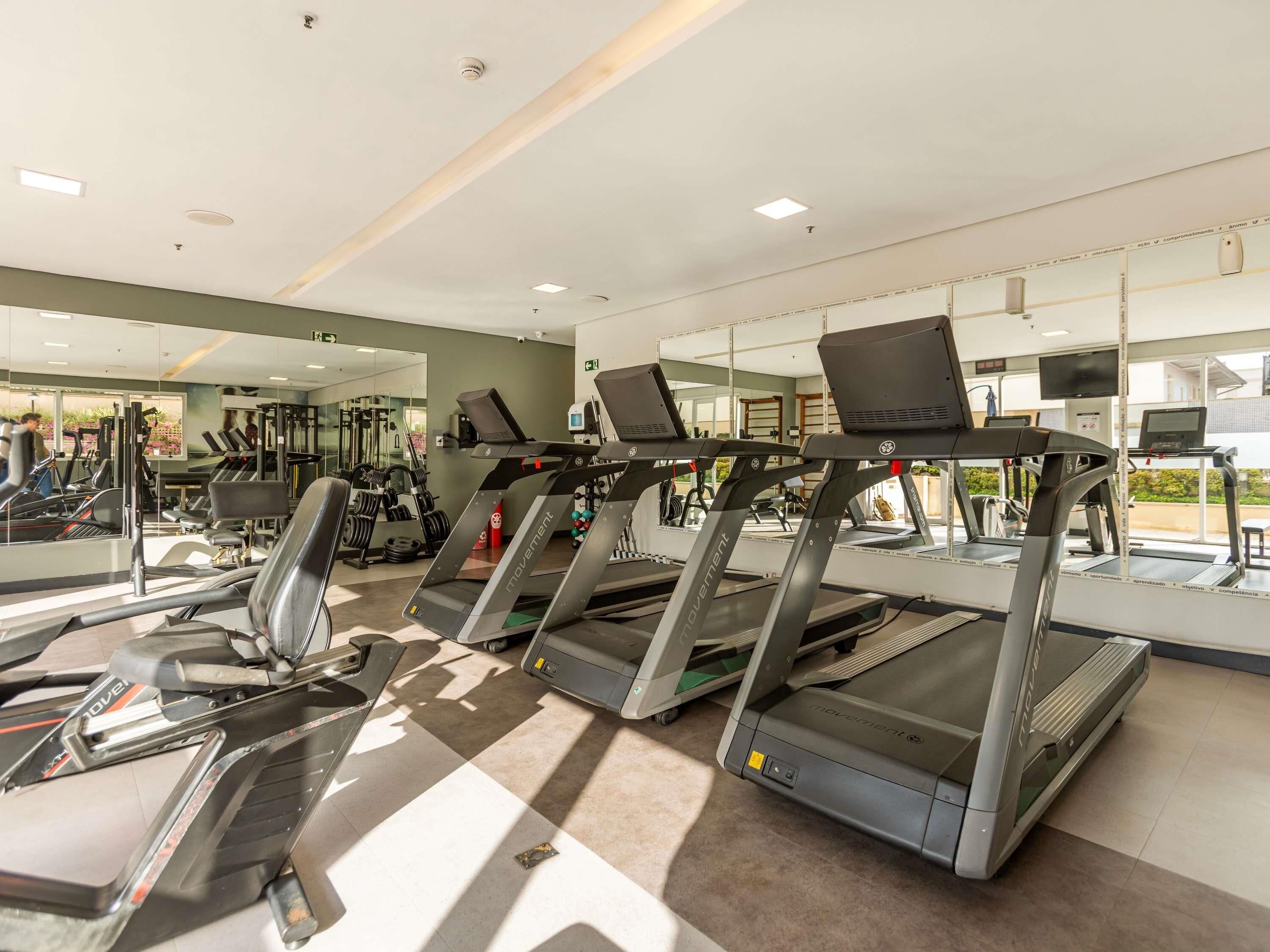 Un gimnasio con cintas de correr, máquinas de pesas y espejos.