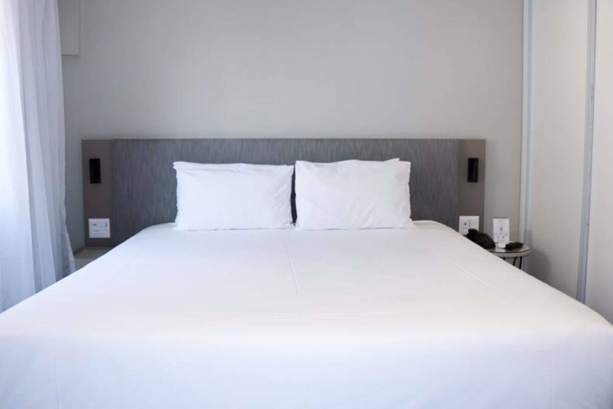 A large bed with white linens, a grey headboard, and bedside tables with lamps.