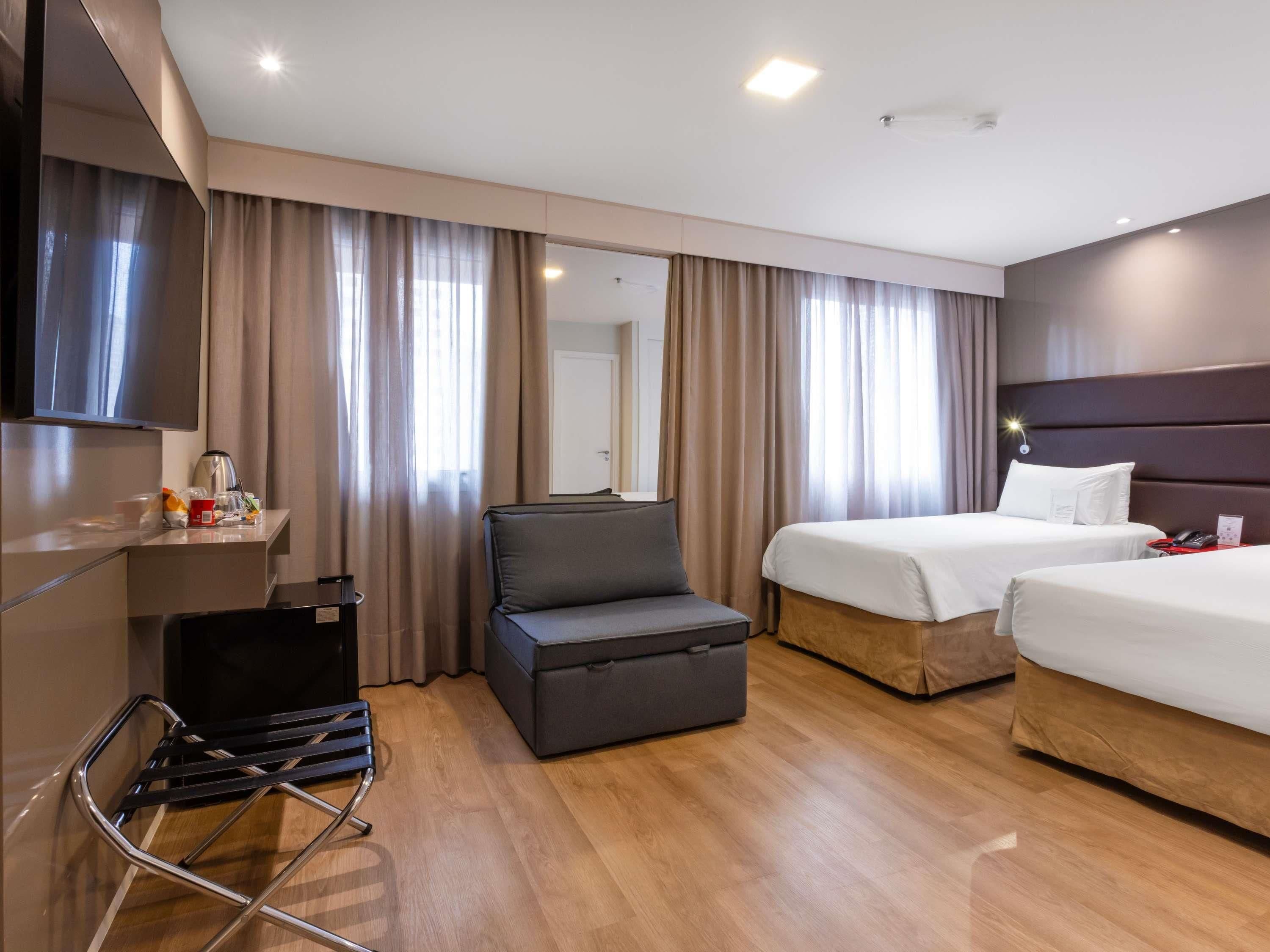 Habitación de hotel con cama, sofá, televisión y escritorio con hervidor.