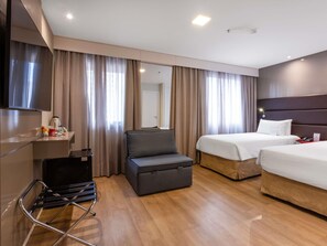 A hotel room with a bed, a sofa, a TV, and a desk with a kettle.